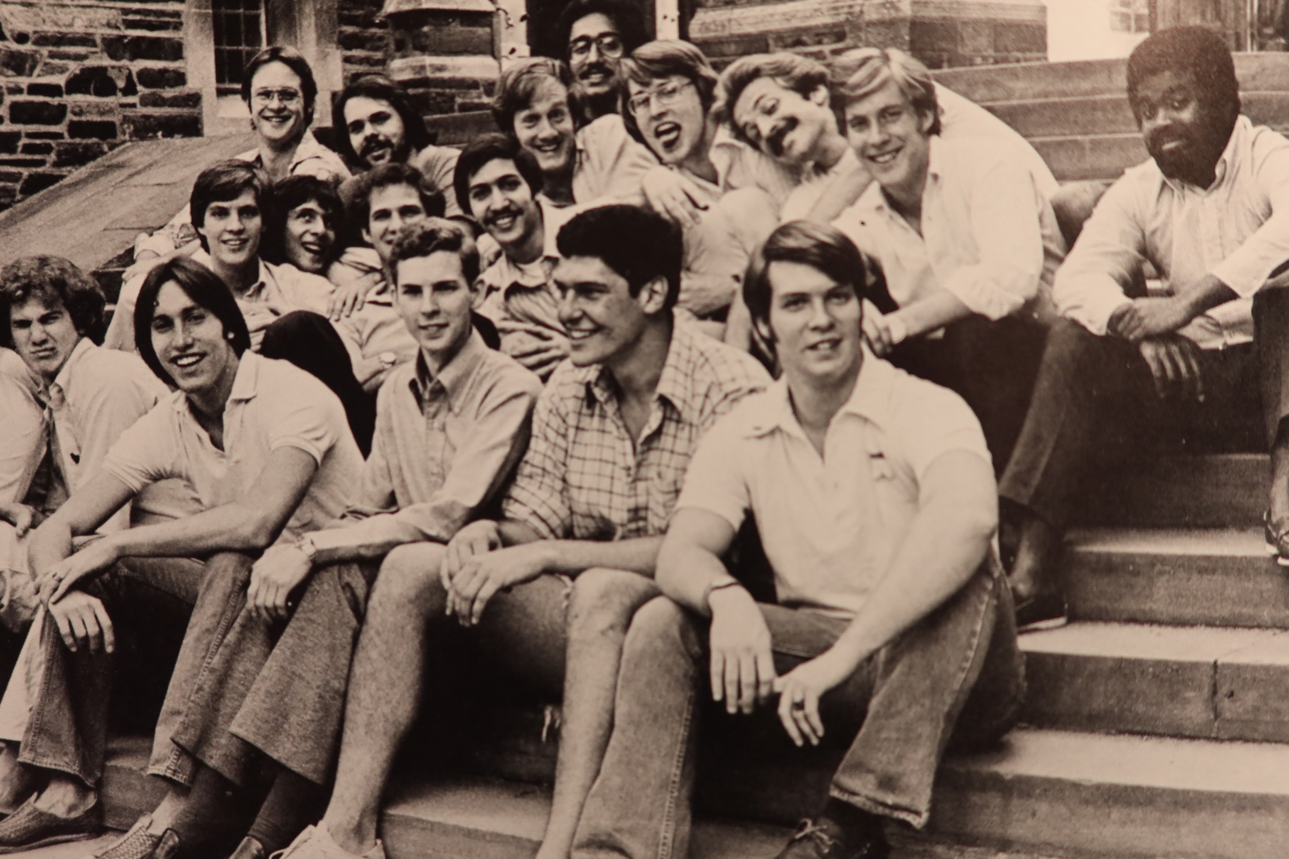 A group of well dressed young men sitting on a stone staircase, some of them acting a bit silly.,