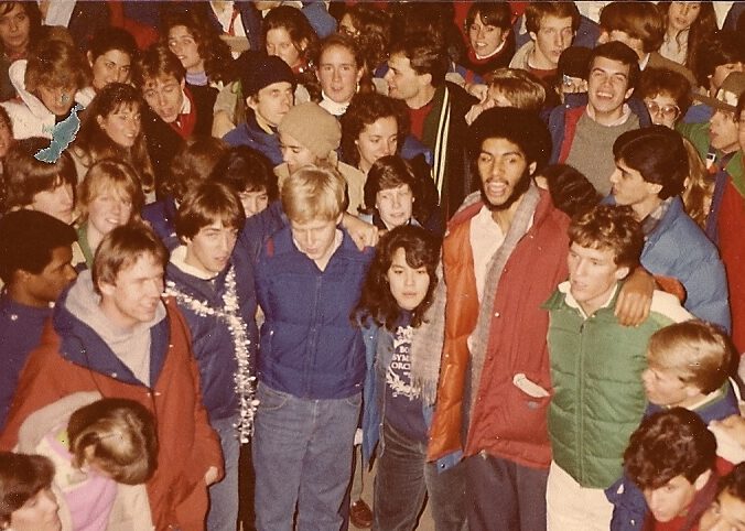 College students outside signing together with their arms wrapped around each other's shoulders.